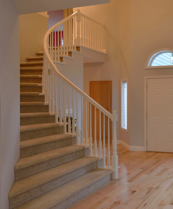 A bright foyer showcasing a recent light hardwood floor installation in Arlington, VA, leading toward a classic curved staircase with white railings and carpeted steps.