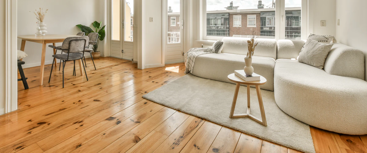 Bright, modern living room featuring a natural wide-plank knotty pine hardwood floor, a white curved sofa, and large windows.