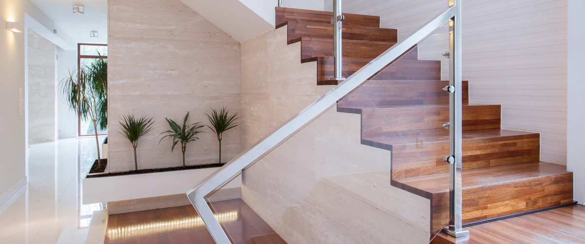 Contemporary interior stair featuring distinct zig-zag wooden treads, a clear glass railing secured with stainless steel hardware, and an adjacent stone accent wall with indoor plants.