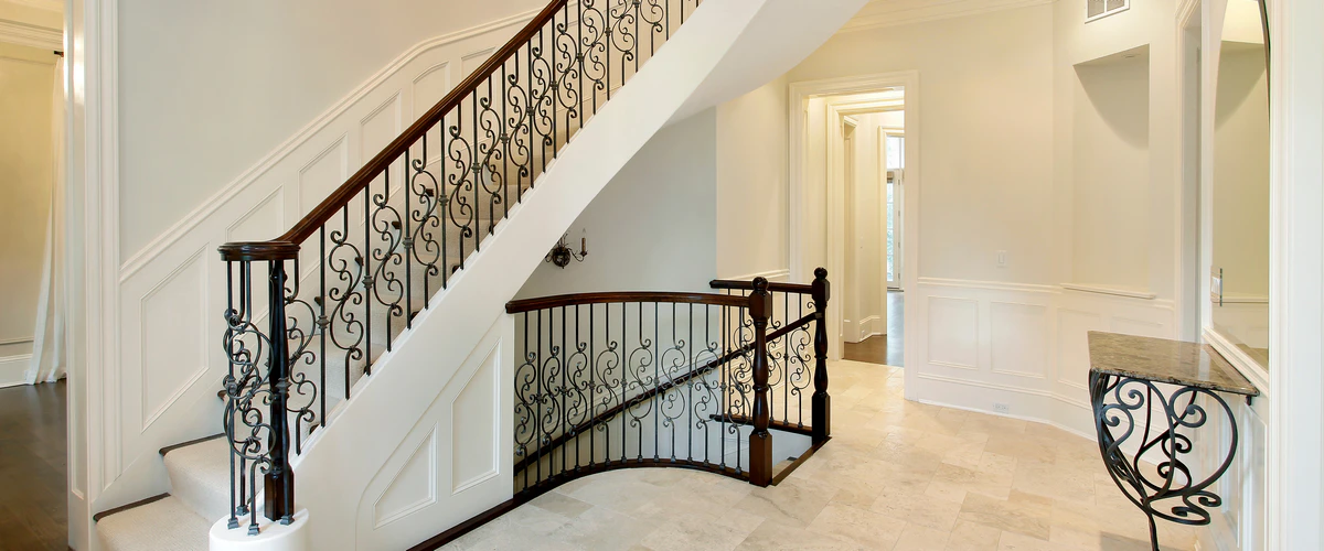 An elegant curved stair railing featuring ornate black wrought iron scrollwork and a rich dark wood handrail in a traditional home interior.