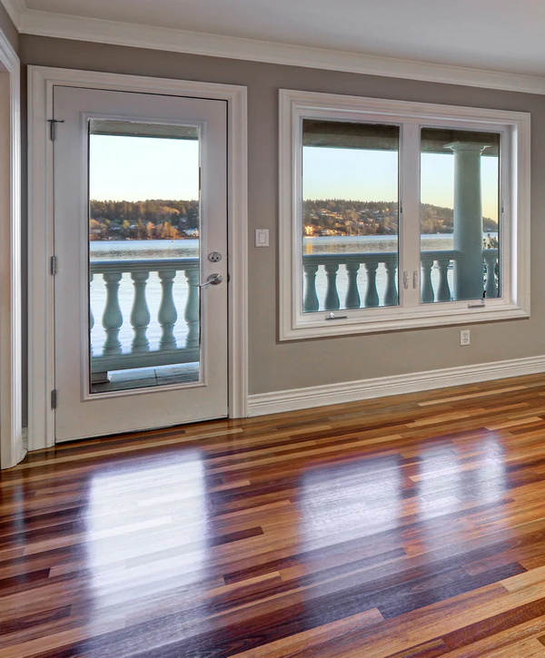 Glossy multi-toned hardwood floor installation in a McLean, VA home featuring large windows and a glass door with a waterfront view.