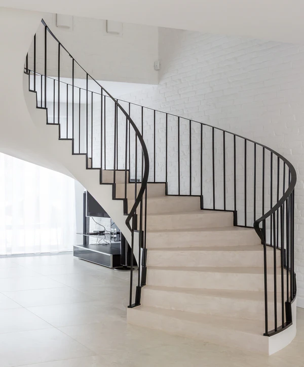 A modern curved stair design featuring light beige steps and a continuous black metal vertical railing inside a bright, white-brick home in Falls Church, VA.