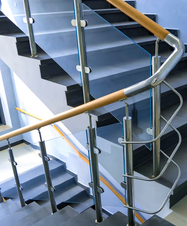 Close up of a modern stair railing installation in Falls Church, VA, featuring clear glass panels, stainless steel hardware, and a smooth wood handrail over dark grey stone steps.