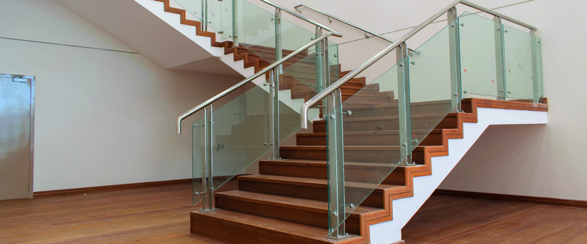 Modern commercial glass panel stair railing with stainless steel handrails and fittings on wide wooden steps.