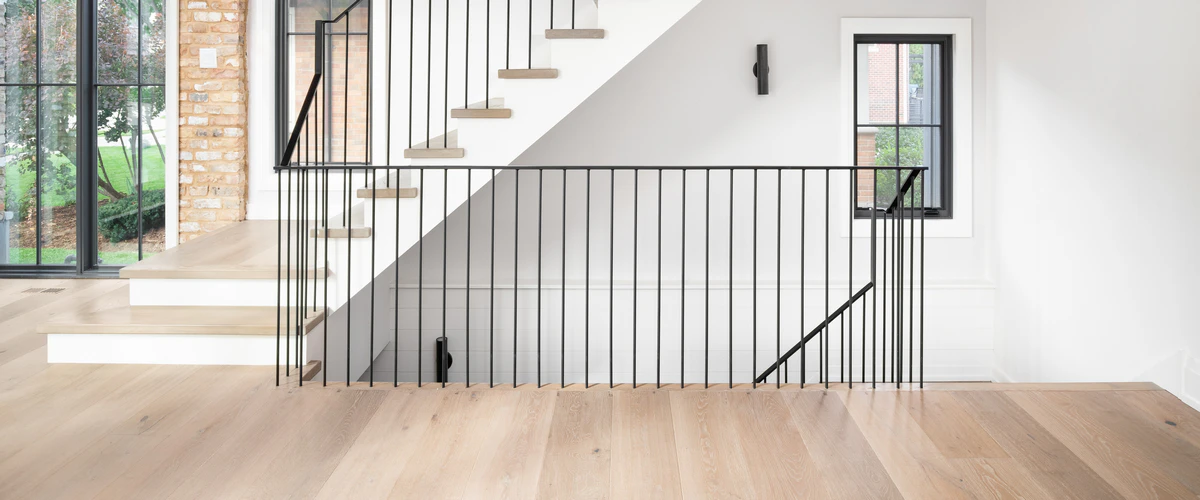 Modern bright entryway featuring a white staircase with thin black metal railings meeting a wide plank light hardwood floor.