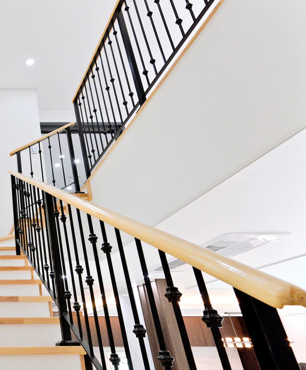 Stair Railing Installation in Alexandria, VA 1 A low-angle view of a multi-level modern staircase featuring light wood treads, white risers, and a professional stair railing installation in Alexandria, VA utilizing black metal balusters with decorative nodes and a light wood handrail.