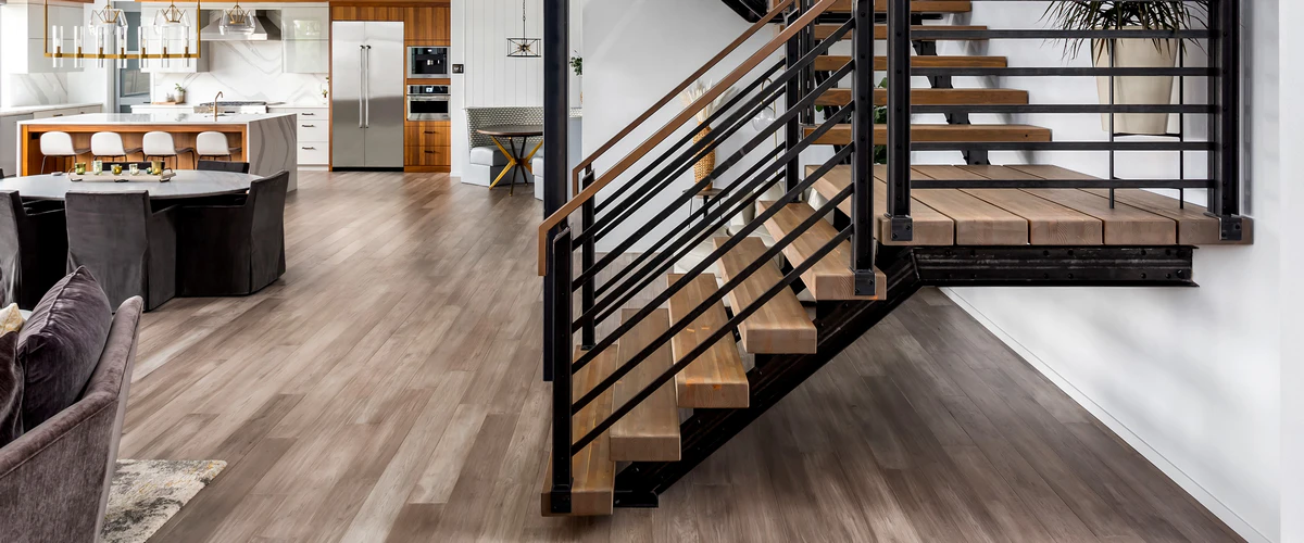 Industrial open riser wood and metal staircase situated over a grey-brown hardwood floor in an open concept modern living and dining area.