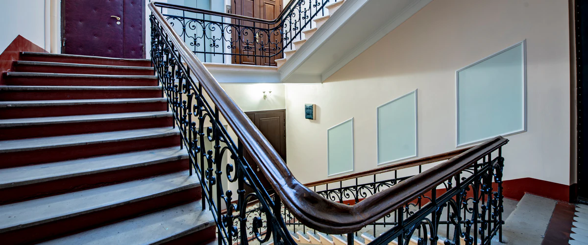 Stair Railing Installation in Alexandria, VA 15 A classic staircase in a building hallway showcasing an intricate, ornate wrought iron scrollwork railing paired with a dark, polished, curved wooden handrail alongside stone steps.