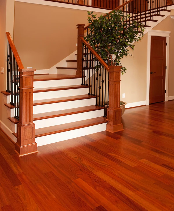 A foyer featuring a new reddish-brown hardwood floor installation and matching staircase with white risers and wrought-iron balusters in Falls Church, VA.