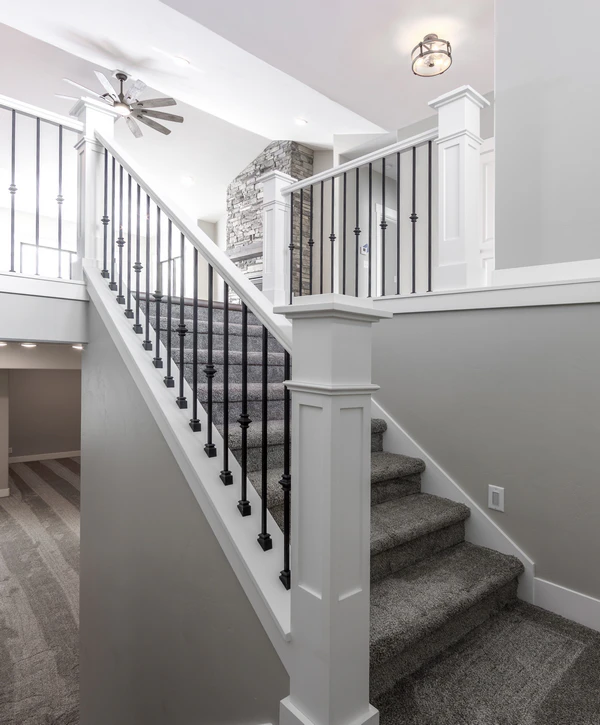A completed residential stair repair in Fairfax, VA, featuring gray carpeted treads, crisp white wooden newel posts, and sleek black iron balusters leading to an upper floor.