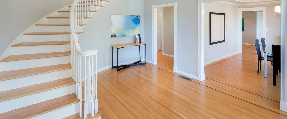 A traditional curved stair featuring natural wood treads, white risers, and a classic white wooden balustrade located in a spacious entryway.