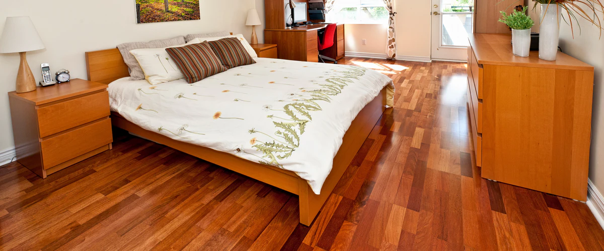 Cozy bedroom interior highlighting a warm, cherry-toned hardwood floor with matching wooden dressers and a bed frame.