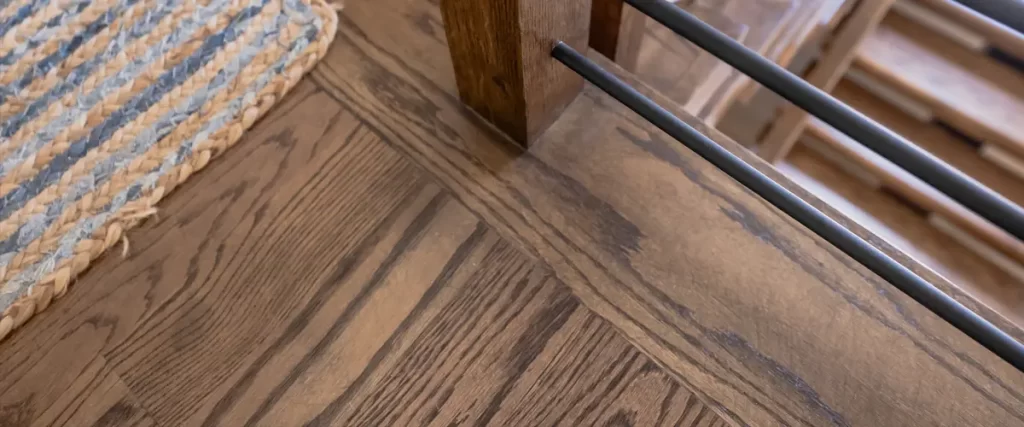 Solid vs Engineered Hardwood Flooring: The Honest Breakdown 2 Custom wood stair railing with black metal balusters and stained hardwood flooring detail