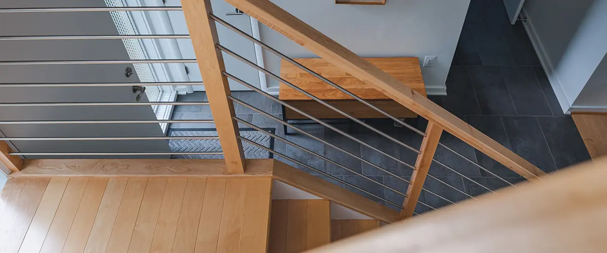 Custom wood stair railing with horizontal metal balusters overlooking modern entryway interior