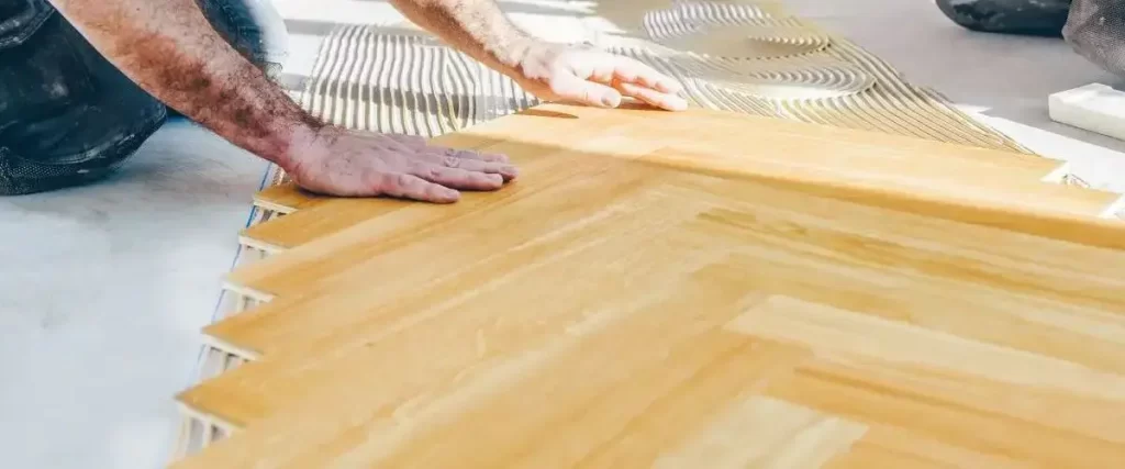 How to Acclimate Hardwood Flooring (Without Wrecking Your Floor) 3 Installer laying herringbone hardwood flooring with adhesive for custom floor renovation