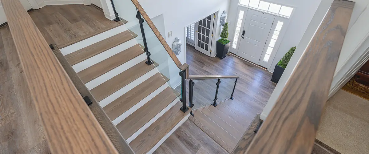 Modern staircase with glass panel railing and hardwood flooring in bright entryway